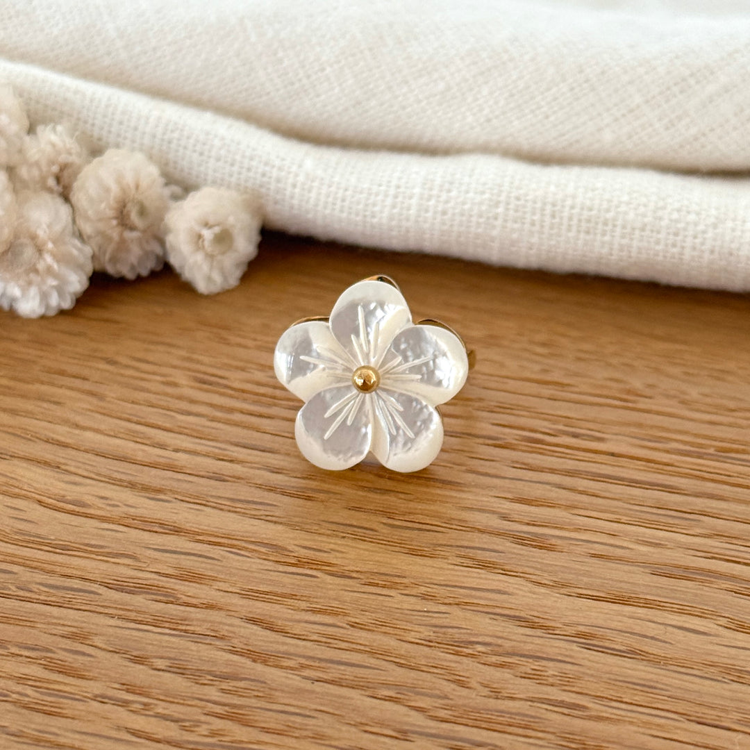 Bague fleur en nacre blanche avec détail doré au centre, montée sur un anneau doré en acier inoxydable.