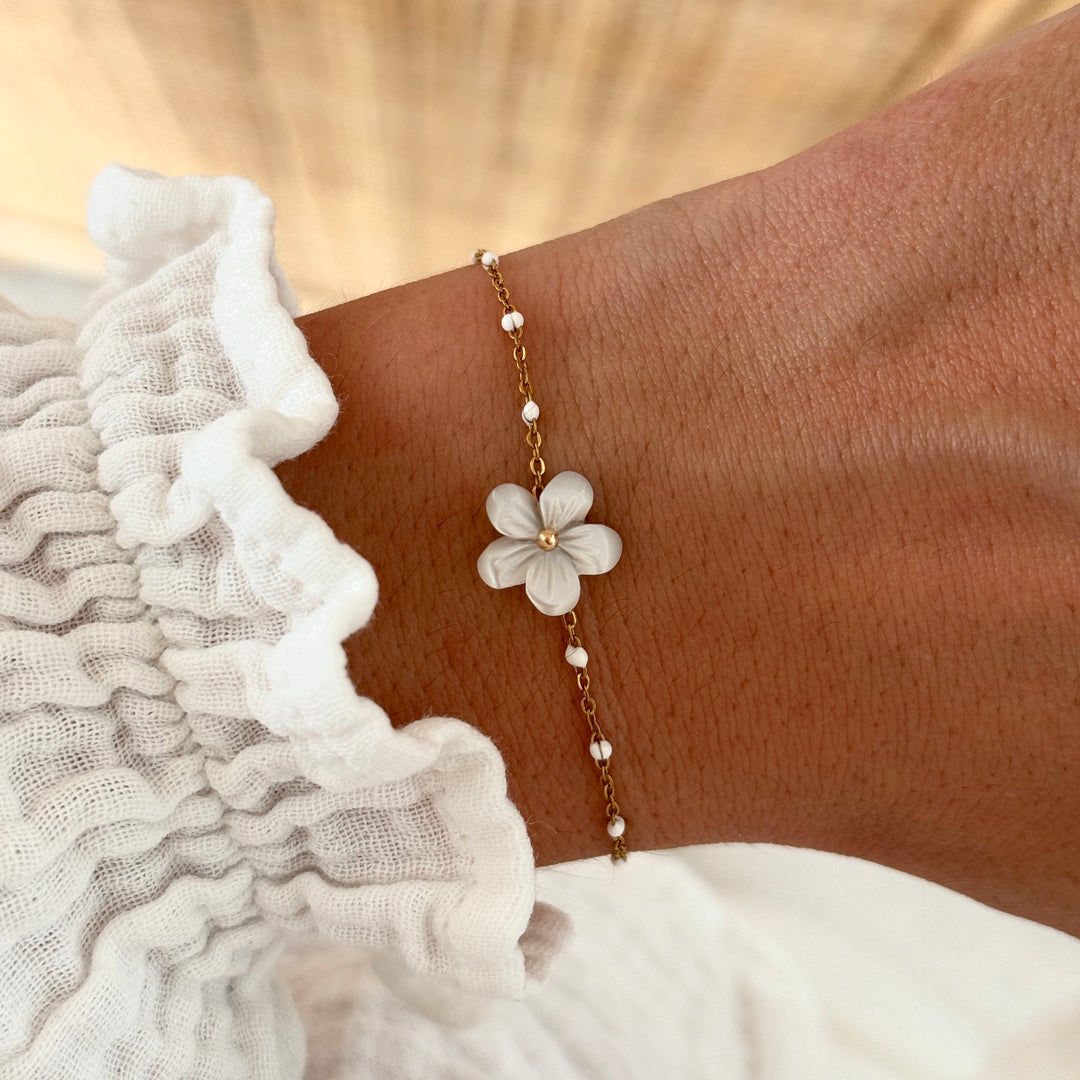 Bracelet en acier inoxydable fin emaillé de petite billes blanches et d’une fleur blanche au centrale.
